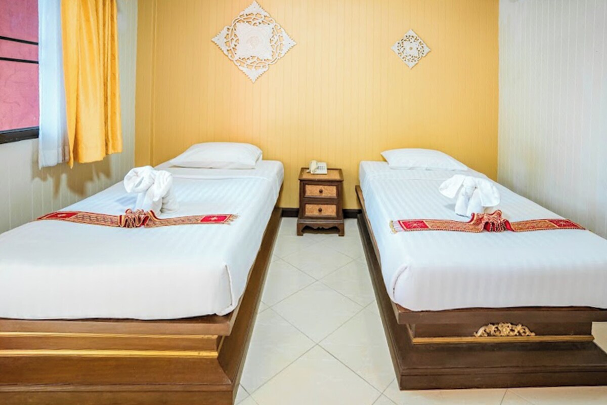 A hotel room with two single beds, a small wooden nightstand, and decorative wall hangings.