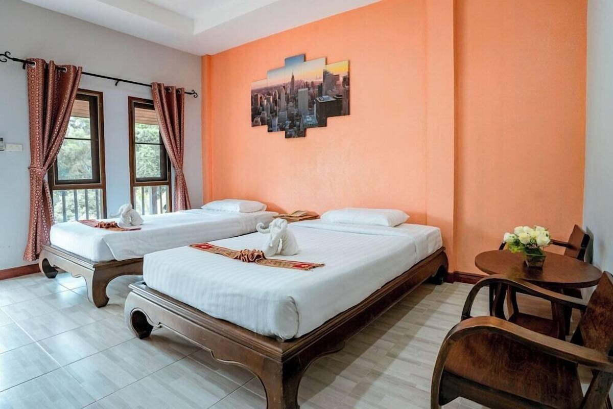 Habitación de hotel con dos camas, una mesa de comedor y una obra de arte con una vista urbana en la pared.