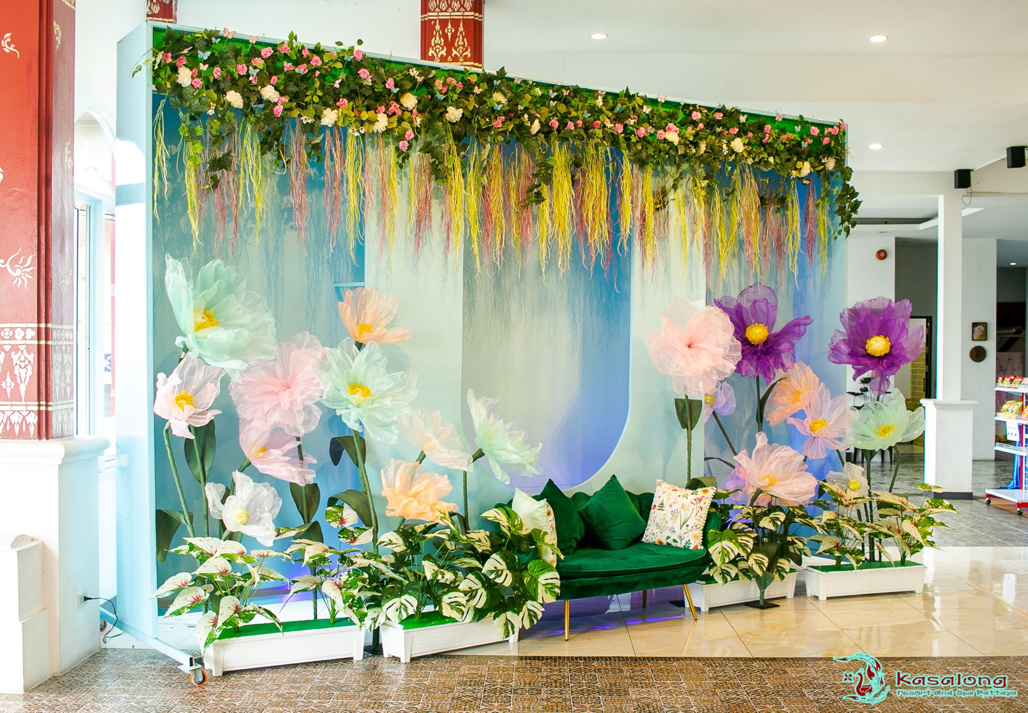 A reception area with a green sofa, potted plants, and a decorative backdrop with hanging flowers.