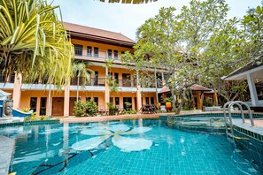 A hotel with a swimming pool, multiple balconies, and tropical landscaping.