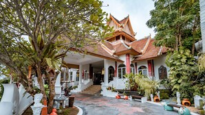 Un edificio tradicional con un techo empinado, una escalera central y un patio con estatuas y plantas.