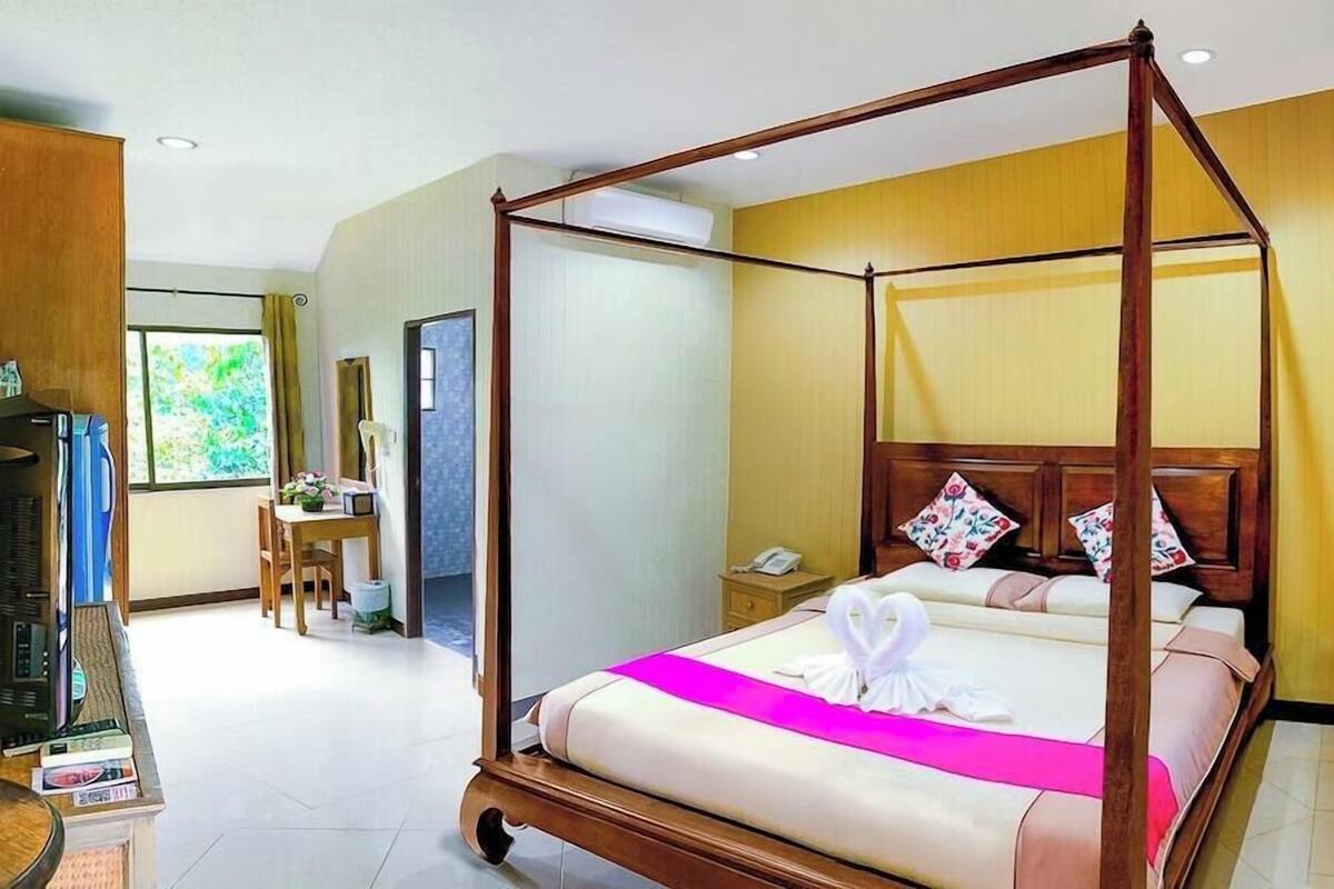 Una cama con dosel, con una colcha rosa y una toalla con forma de cisne, un escritorio de madera con una silla, un teléfono y un espejo en la pared.