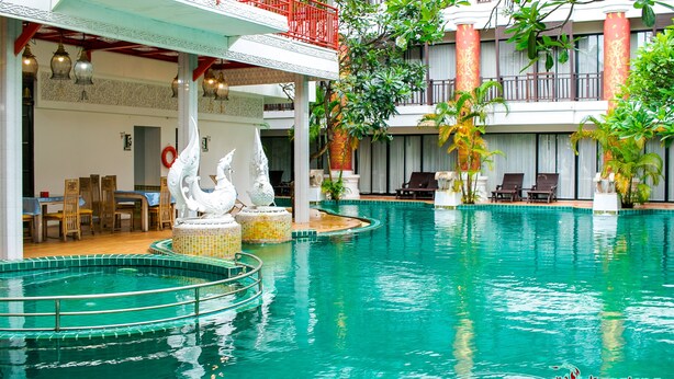 Una piscina interior con zona de estar techada, sillones reclinables y estatuas decorativas.