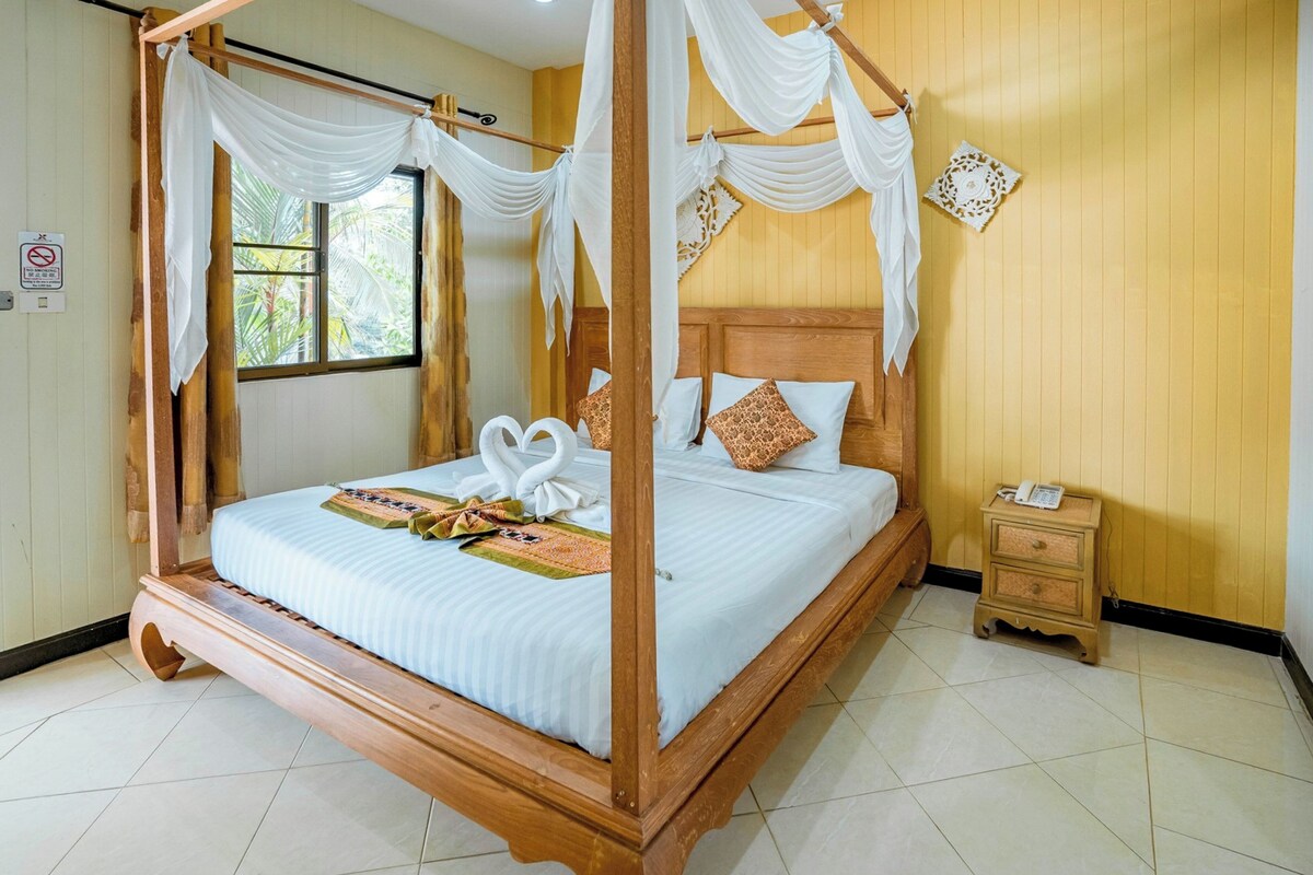 A four-poster bed with white drapes, a wooden headboard, and two pillows.