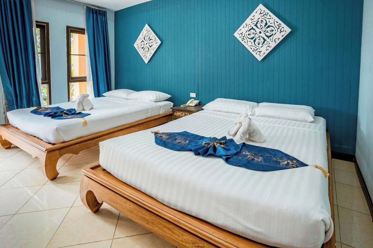 Una habitación de hotel con dos camas de madera, ropa blanca y una pared azul con motivos decorativos.