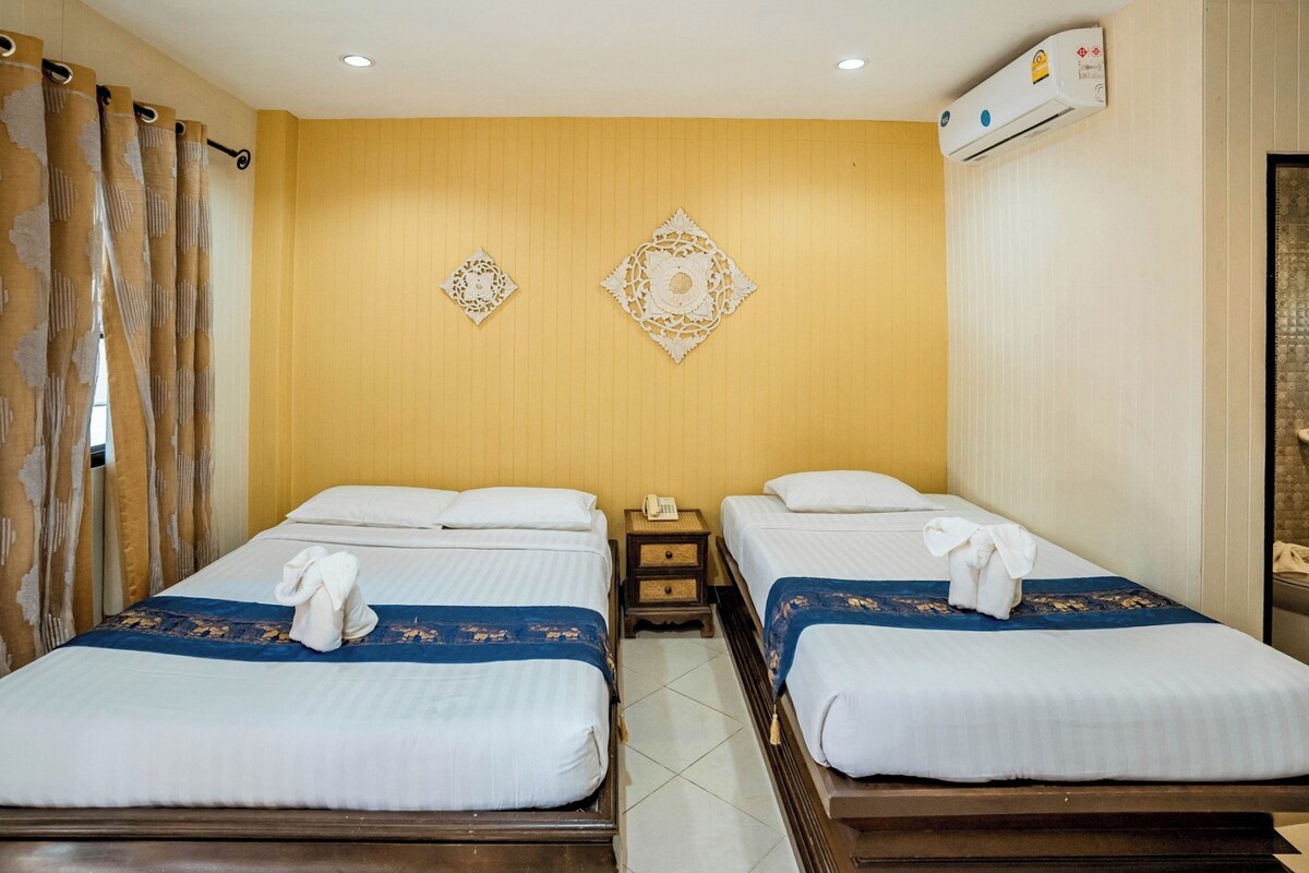 A hotel room with two beds, a wooden floor, a wall-mounted air conditioner, and decorative wall art.