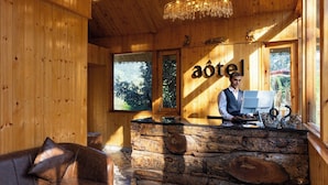 A wooden interior with a reception desk, a receptionist, and a view of the outdoors. - Aotel Pangot (Formerly Royal Cliff) (Nainital)