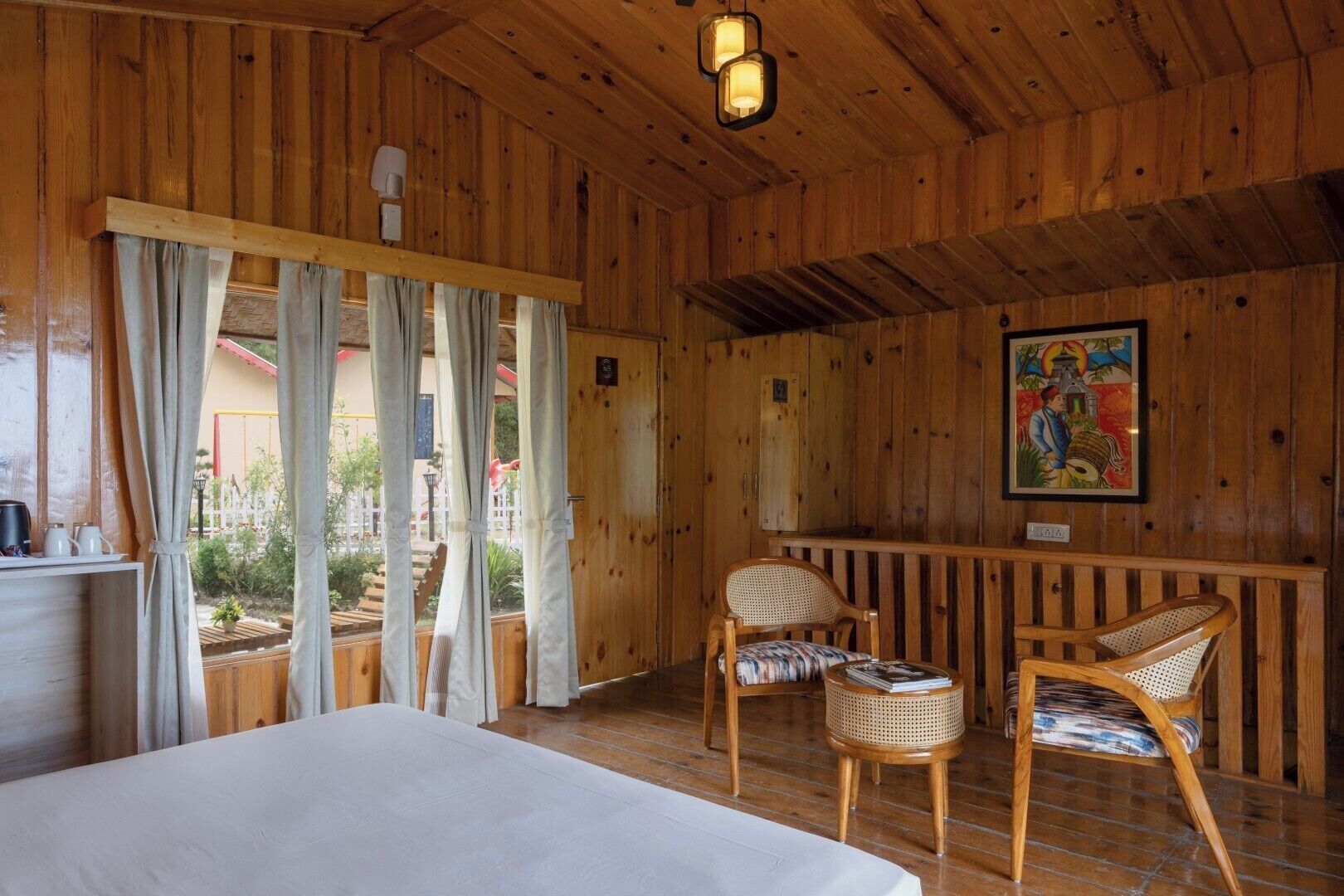 Une pièce en bois avec un lit, deux fauteuils en osier, une petite table et un tableau accroché au mur.