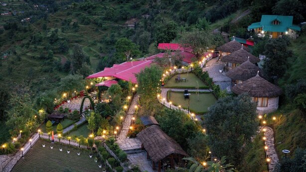 A rural village with traditional thatched-roof houses, a central paved area with seating, and a surrounding garden. - Aotel Pangot (Formerly Royal Cliff) (Nainital)