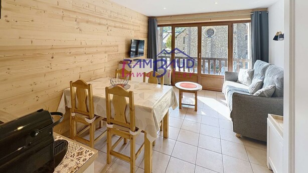 A room with a wooden wall, a dining table with chairs, a sofa, a TV, and a balcony with a view. - Studio Cabin in center Valloire with Free Wifi (VALLOIRE)