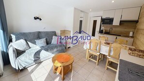 A modern living room with a grey sofa, wooden dining table, and a kitchen area. - Studio Cabin in center Valloire with Free Wifi (VALLOIRE)