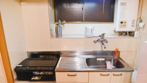 A compact kitchen with a stove, sink, and a window above the counter. - North Shinjuku house (Tokyo)
