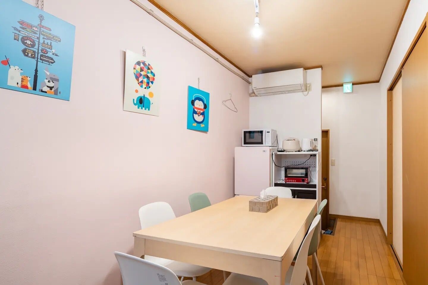 A small, modern room with a wooden table and chairs, a microwave, a mini-fridge, and a wall-mounted air conditioner.
