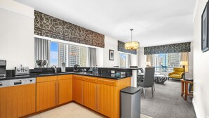 A modern kitchen with wooden cabinets, a black countertop, and a built-in oven. There is a dining area with a yellow chair and a table.