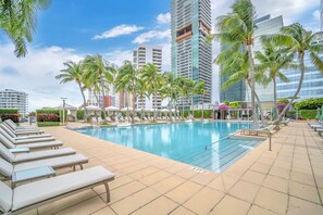A swimming pool with lounge chairs, palm trees, and modern buildings in the background. - Luxury 2BR/2BA City View Suite (Miami)