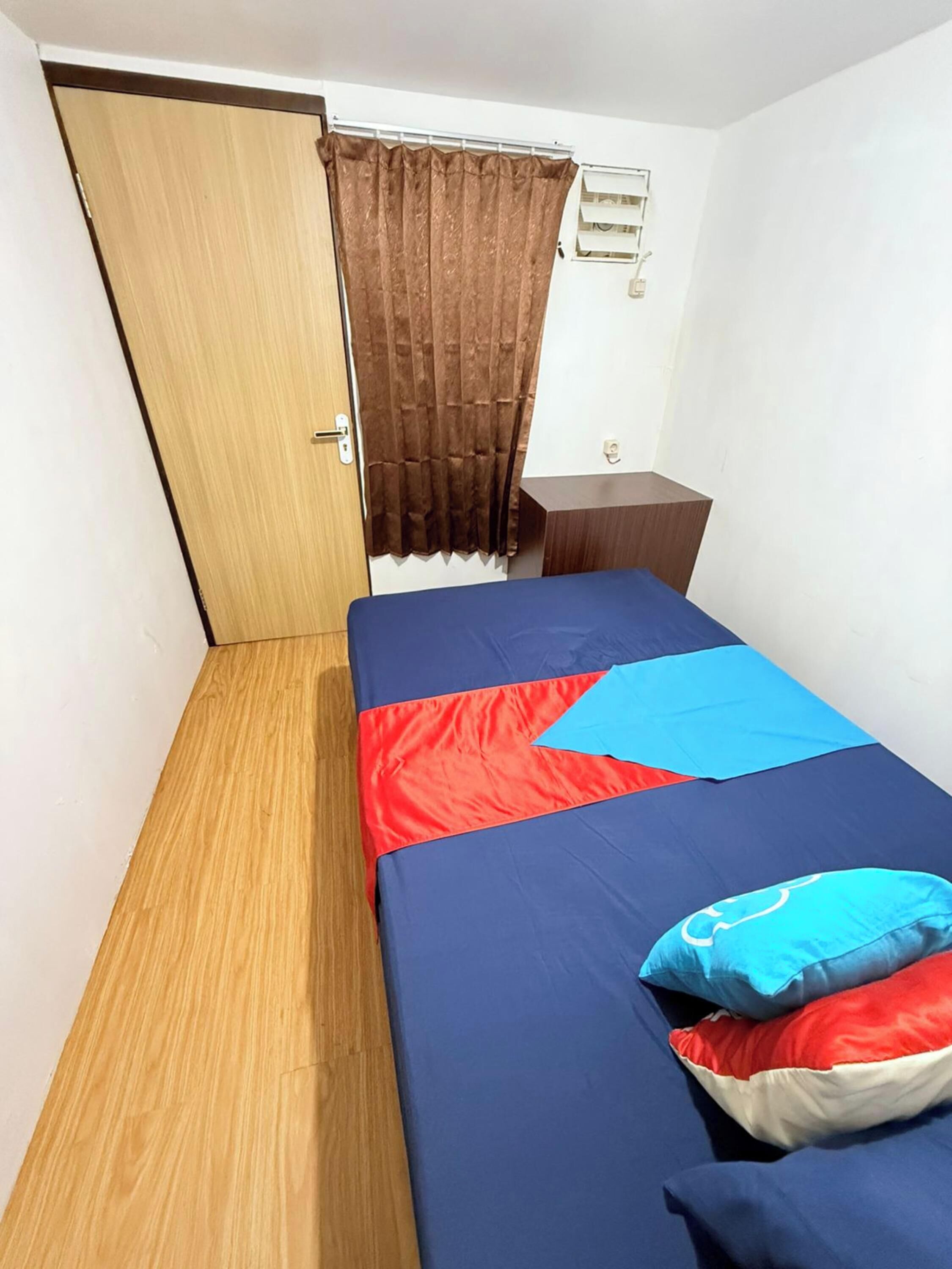 A room with a bed, a wooden door, a small bedside table, and a window with curtains.