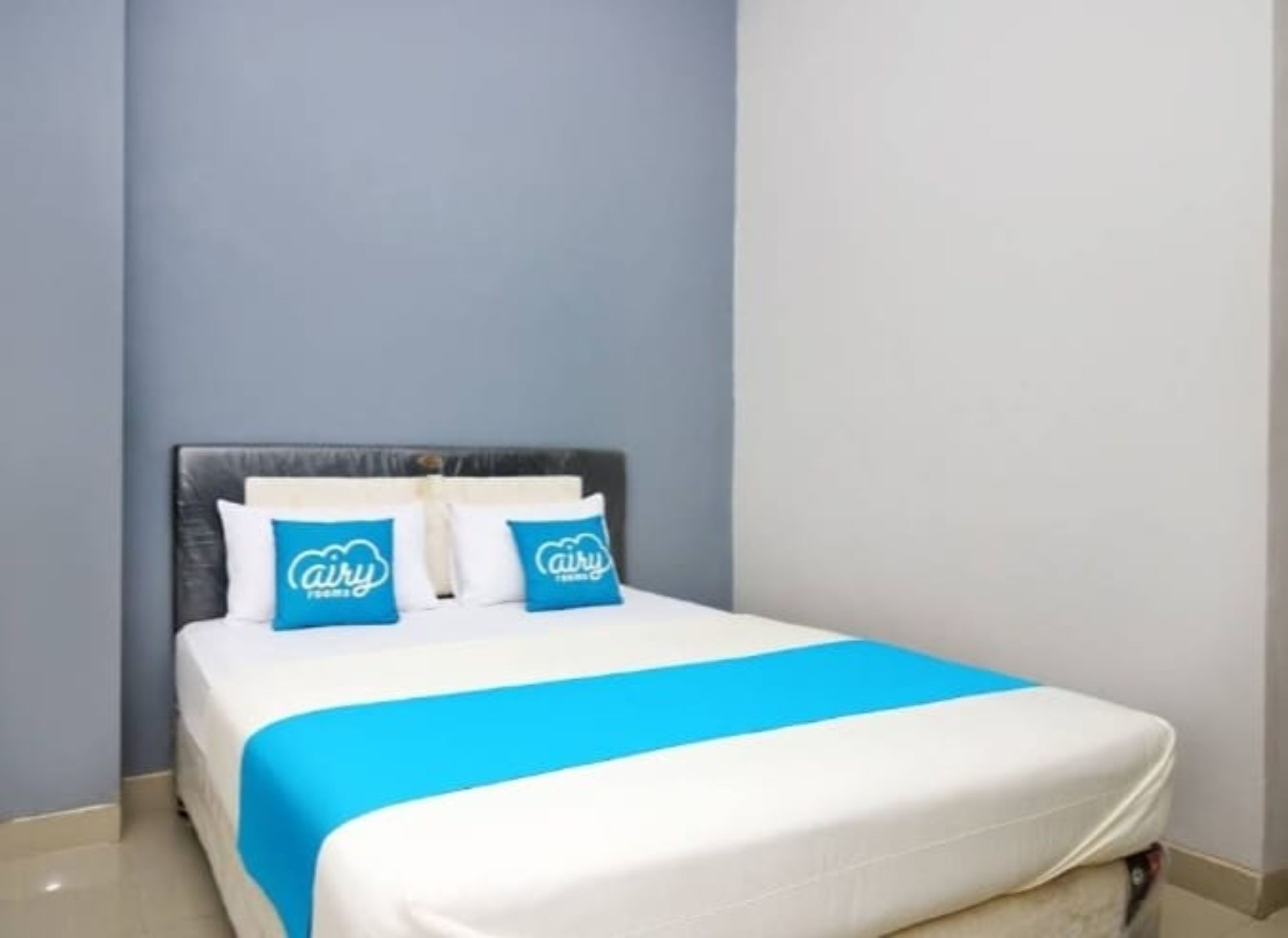 Habitación de hotel con cama, dos almohadas de la marca 'airy' y una colcha azul y blanca.