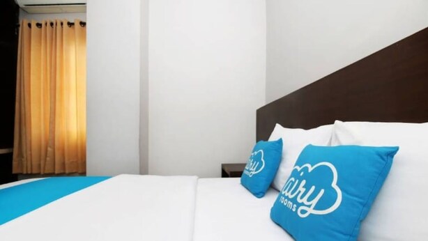 A hotel room with a bed, two pillows with a logo, a nightstand, and a window with curtains. - Ambon Residence Syariah (Ambon)