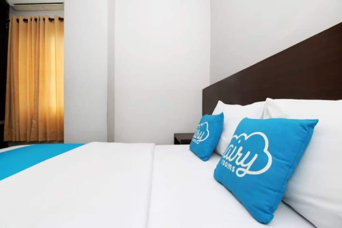 A hotel room with a bed, two pillows with a logo, a nightstand, and a window with curtains.