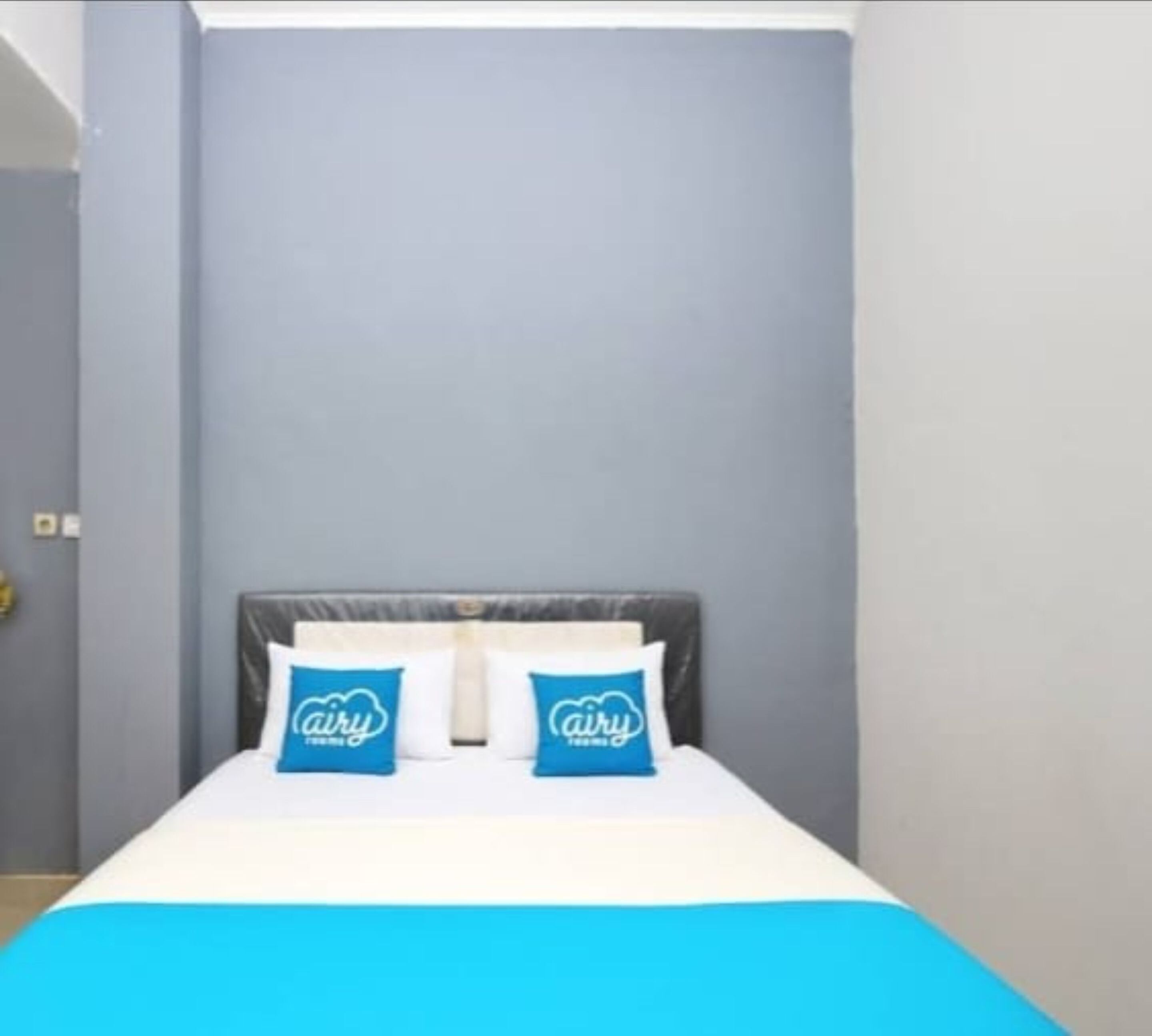 A bed with a grey headboard, white bedding, and two blue pillows with the 'airy' logo.