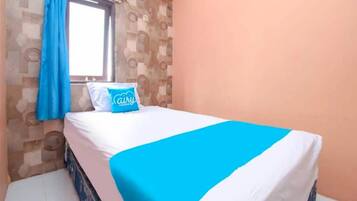 Un letto singolo con copriletto bianco e blu, un cuscino con la scritta "Cairu Room" e una finestra con tende blu.