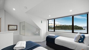 A hotel room with two beds, a large window with a view of a lake and mountains, and a glass partition wall.