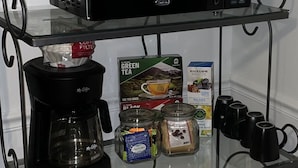 Un plan de travail de cuisine avec une machine à café, un bocal de café, une boîte de thé vert et un four à micro-ondes.
