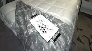 Un lit bien fait, avec une couette blanche et une petite pancarte indiquant «merci», un tableau accroché au mur et une lampe placée sur la table de chevet.