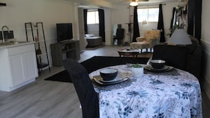 Un salon avec une table à manger dressée pour deux personnes, un canapé et un téléviseur en arrière-plan.