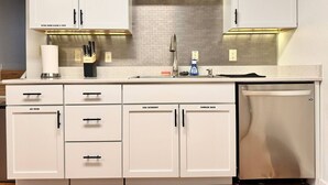 A modern kitchen with white cabinets, a stainless steel dishwasher, and a tiled backsplash. - Blue House Retreat 2 (Sioux Falls)