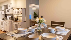 A modern kitchen with white cabinets and a dining area with a wooden table set for four. - Blue House Retreat 2 (Sioux Falls)