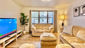 A living room with a flat-screen TV, a beige sofa, a matching armchair, a wooden coffee table, and a potted plant. - Blue House Retreat 2 (Sioux Falls)