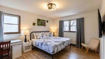A bedroom with a bed, bedside tables, a desk, a chair, and a TV mounted on the wall.