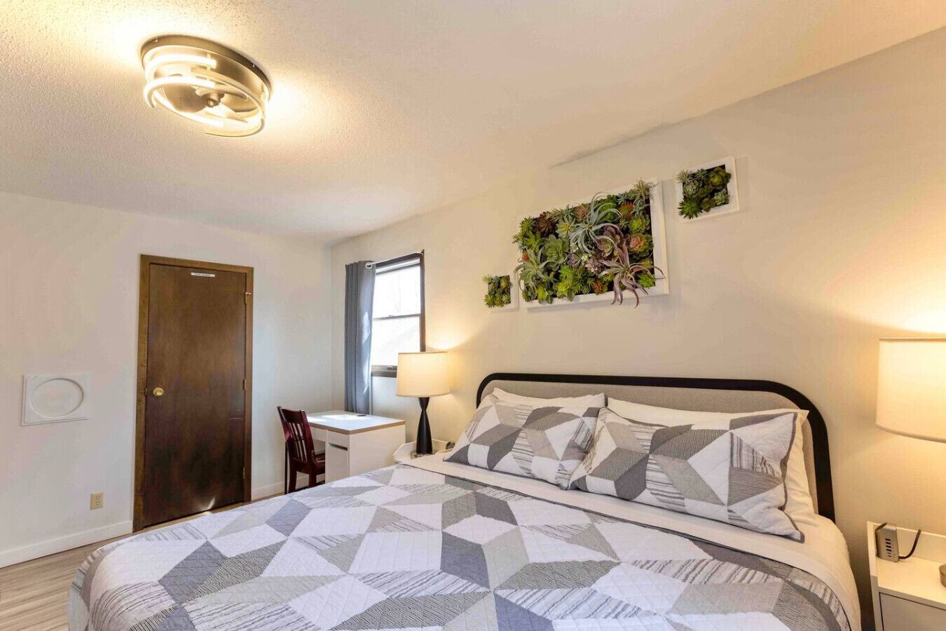 Ein Schlafzimmer mit Bett, Schreibtisch, Stuhl, Fenster und einer Wandpflanze.