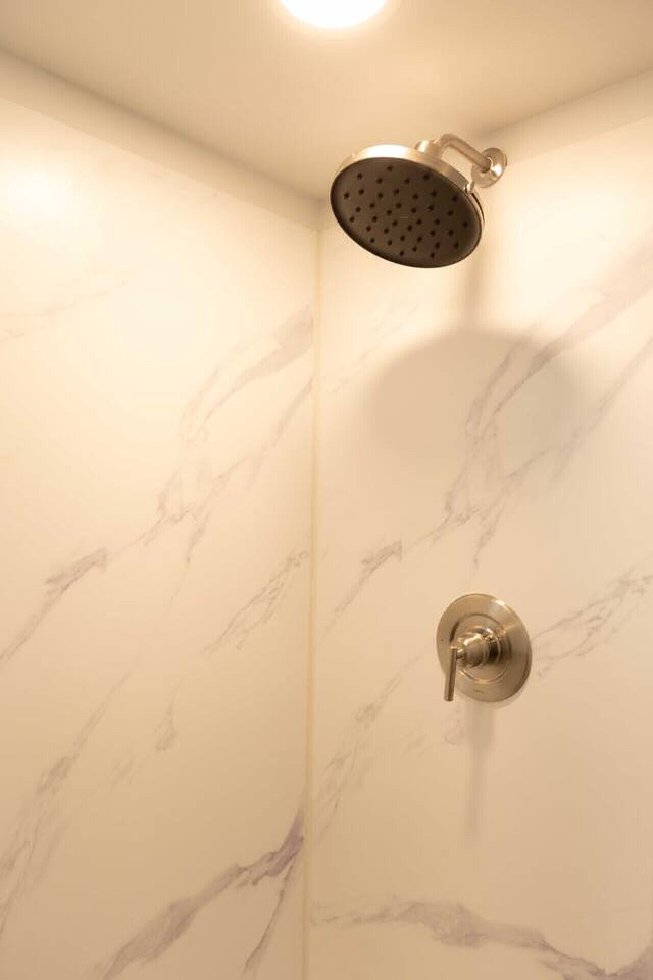 Ducha con cabezal de ducha manual y llave de control empotrada en una habitación con paredes de mármol.