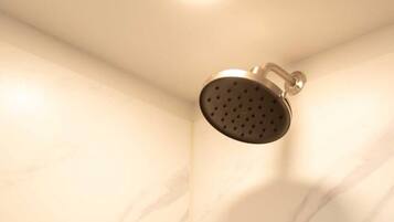 Ducha con cabezal de ducha manual y llave de control empotrada en una habitación con paredes de mármol.