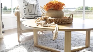 Una habitación con una mesa redonda de madera, un tapete blanco y vistas amplias a través de grandes ventanales.