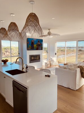 A modern kitchen with a central island, a built-in oven, and a large window overlooking a natural landscape. - Lake House, by the beach (The Honeysuckles)