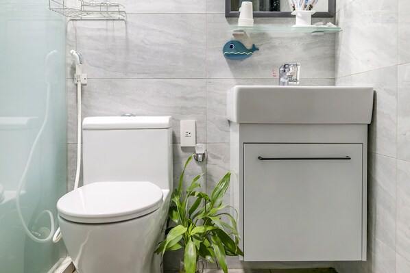 Un baño moderno con inodoro, lavabo, cabina de ducha de vidrio y una planta en maceta.
