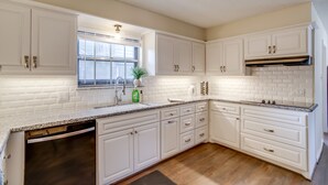 A kitchen with white cabinets, a granite countertop, a dishwasher, and a window with blinds. - Roomy Houston Rental w/ Home Office & Private Pool (Houston)