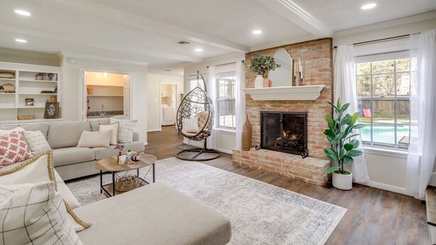 A spacious living room with a fireplace, a hanging chair, and a view of a pool through large windows. - Roomy Houston Rental w/ Home Office & Private Pool (Houston)