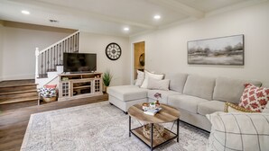 A living room with a sofa, coffee table, TV, and a staircase. - Roomy Houston Rental w/ Home Office & Private Pool (Houston)