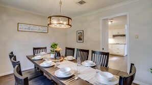 A dining room with a long wooden table set for six, surrounded by dark wooden chairs. A chandelier hangs from the ceiling, and a framed inspirational quote is on the wall. - Roomy Houston Rental w/ Home Office & Private Pool (Houston)
