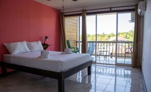 A hotel room with a bed, a desk with a lamp, a chair, and a balcony with a view. - Los balcones over the sea (Bocas del Toro)