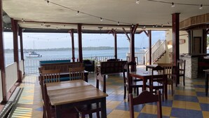 A covered outdoor seating area with wooden tables and chairs, overlooking a body of water with boats. - Los balcones over the sea (Bocas del Toro)