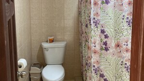 A small bathroom with a toilet, a trash bin, and a shower curtain with a floral pattern. - Los balcones over the sea (Bocas del Toro)