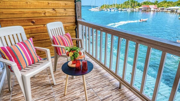 A wooden deck with two white chairs and a small table with a vase of flowers. - Los balcones over the sea (Bocas del Toro)