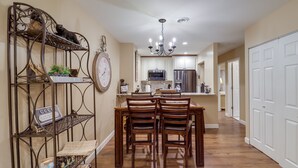 A dining area with a wooden table and chairs, a metal bookshelf, and a kitchen in the background. - Mtn-View Condo w/ Lookout Deck in Banner Elk! (Banner Elk)