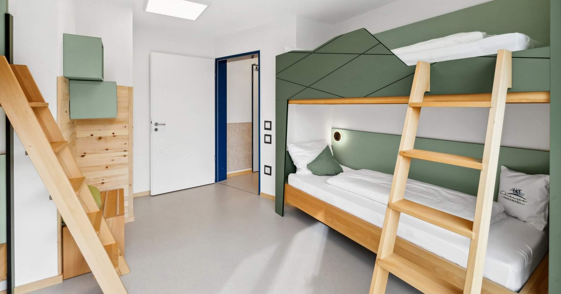 Ein Schlafraum mit Etagenbetten, einer Holzleiter, einer weißen Tür und einer grünen Wand.