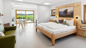 Un dormitorio moderno con cama de madera, sofá verde y zona de comedor con vistas al exterior.